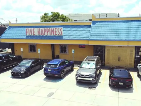 Storefront of Five Happiness (五福) at 3605 S Carrollton Ave, New Orleans — a yellow building with a blue tile roof, lion statue, and lit OPEN sign above the parking lot