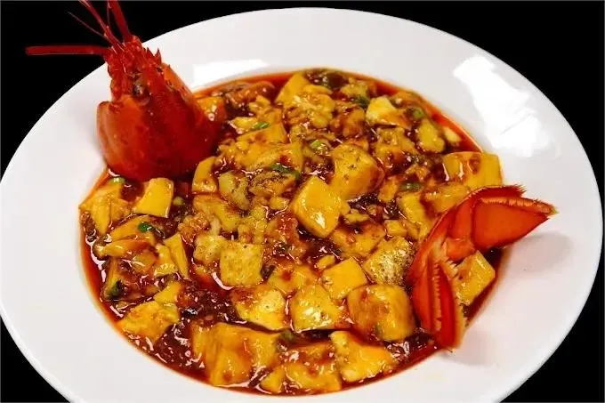 Signature Sichuan mapo-style tofu in red chili-oil sauce topped with lobster, plated on a white dish at Chuan Jiang Hao Zi in Columbus
