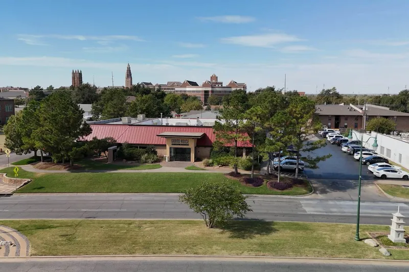 Exterior of Grand House Asian Bistro at 2701 N Classen Blvd in Oklahoma City, a red-roofed building with signage and parking lot, with the OKC skyline behind it