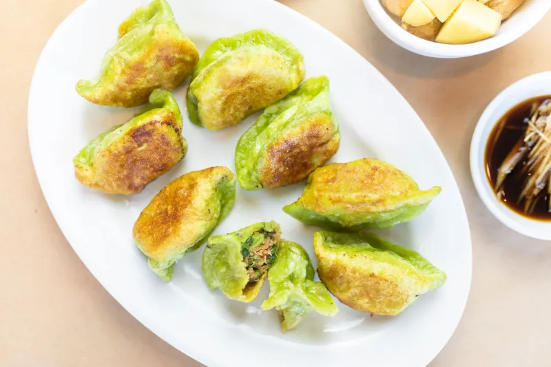 Plate of Katy's Dumplings pan-fried green (vegetable-dough) dumplings with soy dipping sauce