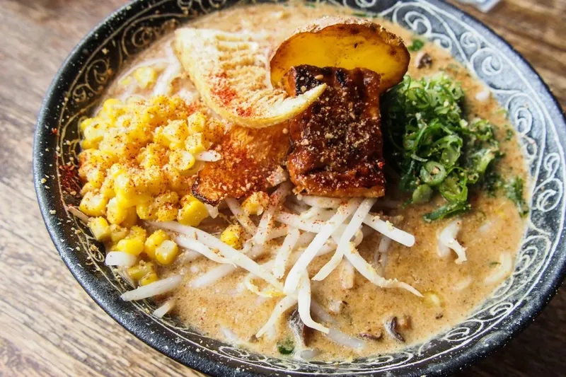 A bowl of Facing East paitan ramen topped with charred char siu, seasoned corn, bean sprouts, scallions and a bamboo shoot in a creamy broth