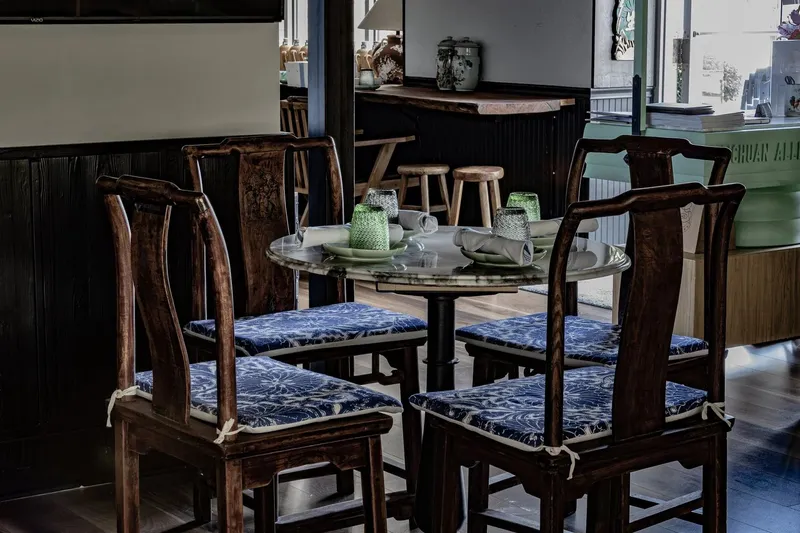 Interior of Sichuan Alley Bistro in West Hartford with a marble-topped table, carved wooden chairs with blue cushions, and the restaurant's branded host stand